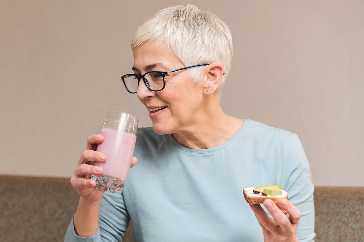 mature woman full of energy drinking healthy fruit smoothie and holding toast with avocado, Healthy nutritious breakfast concept
