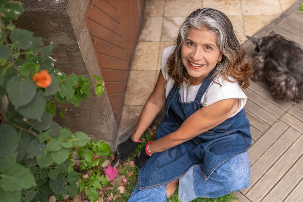 Happy mature woman planting flowers in the garden at home