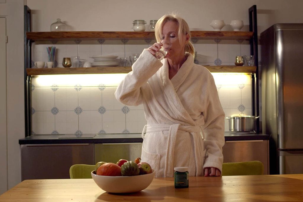 Senior woman in bathrobe taking vitamin pills in kitchen.