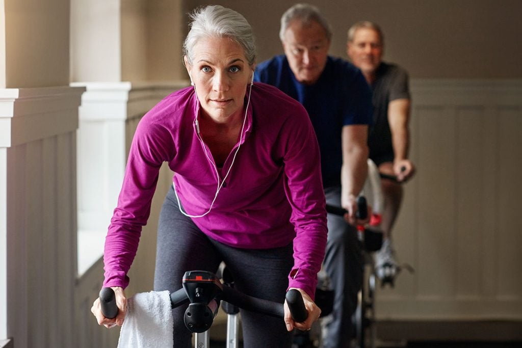Spin class, fitness or senior woman on bike in workout or training for cycling progress, health or wellness. Group, challenge or confident elderly person on bicycle machine for gym or cardio exercise