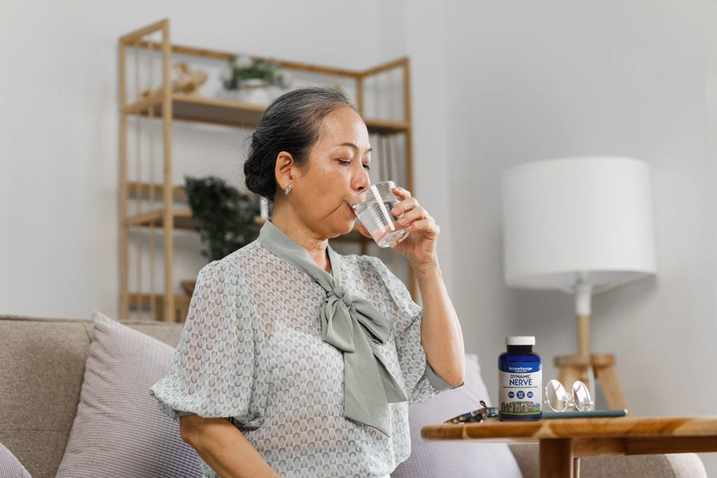 Senoir mature asian woman with glass of water taking pills, sitting on couch.