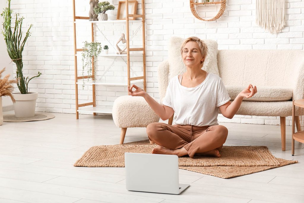 Mature woman with laptop meditating at home.