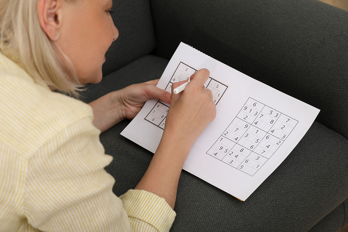 Middle aged woman solving sudoku puzzle on sofa at home