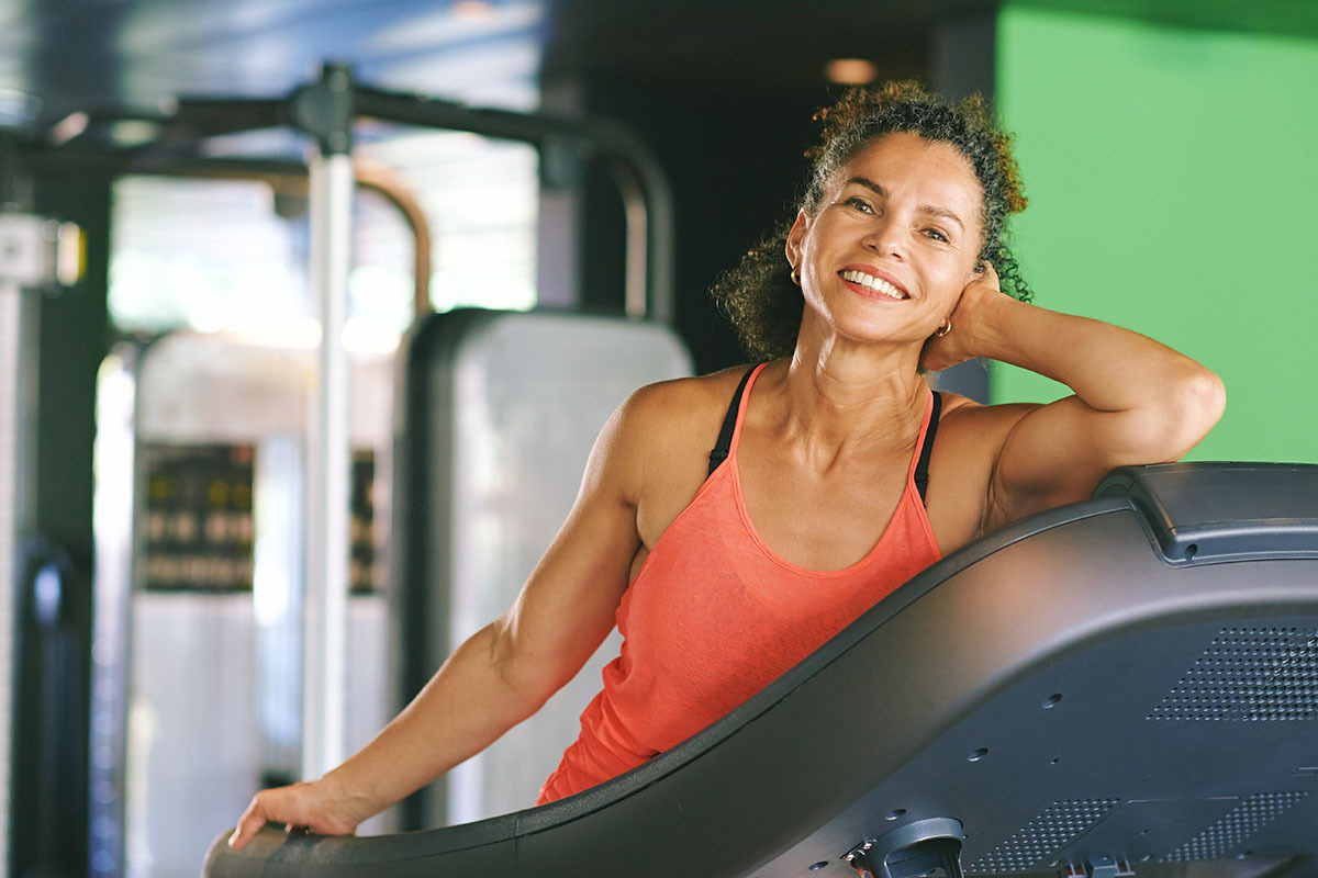 Gym portrait of mature woman leaning on treadmill, active and healthy lifestyle concept