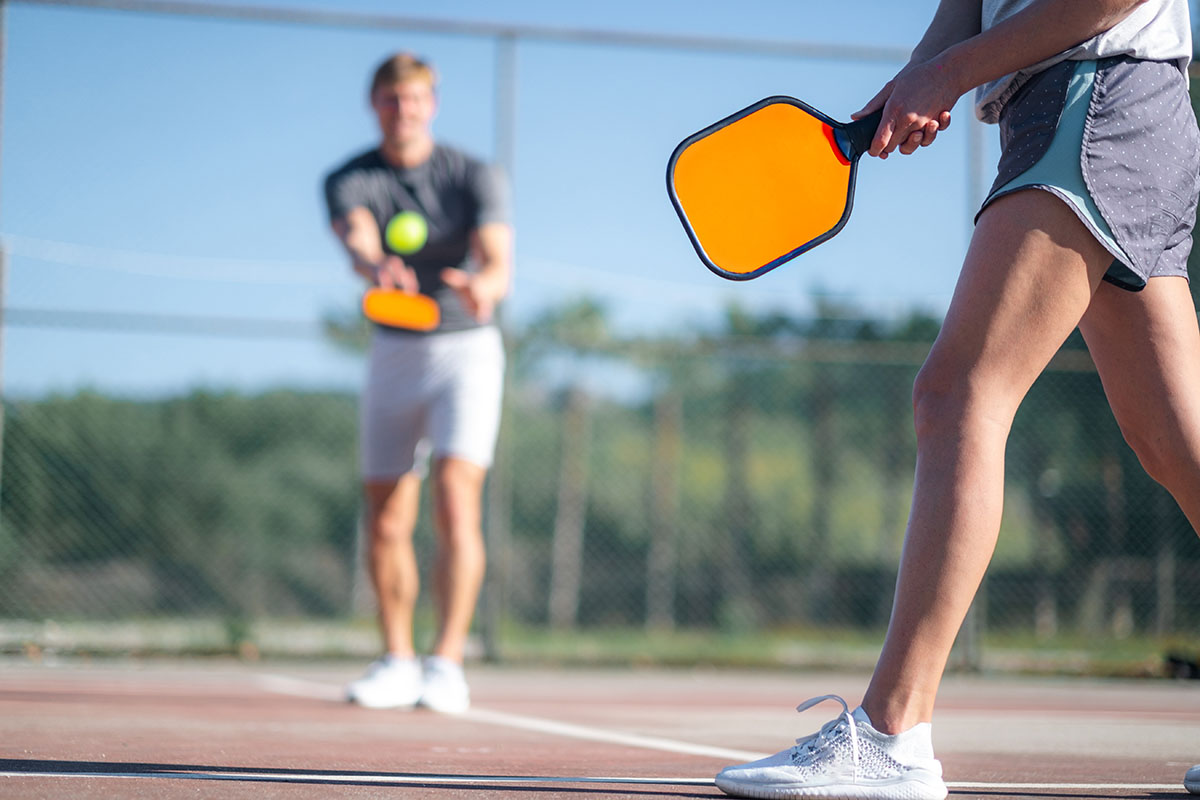 couple playing pickleball game, hitting pickleball yellow ball with paddle, outdoor sport leisure activity.