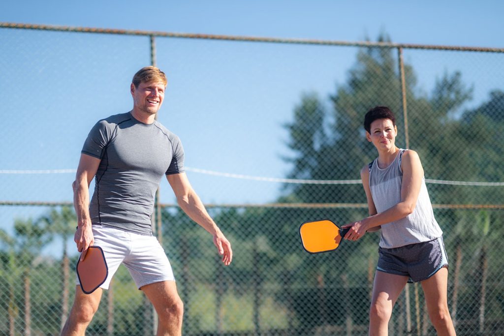 couple playing pickleball game, hitting pickleball yellow ball with paddle, outdoor sport leisure activity.