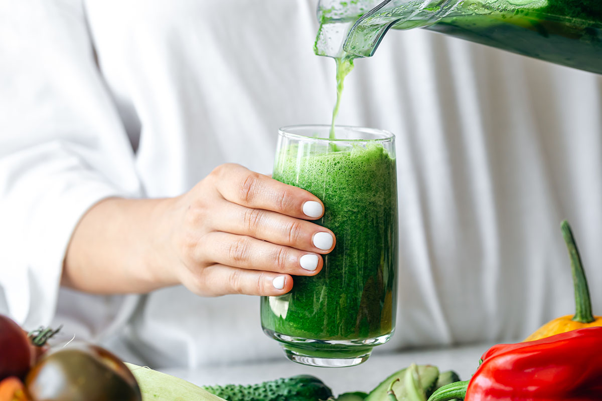 A woman pouring green smoothie to glass, healthy food concept.