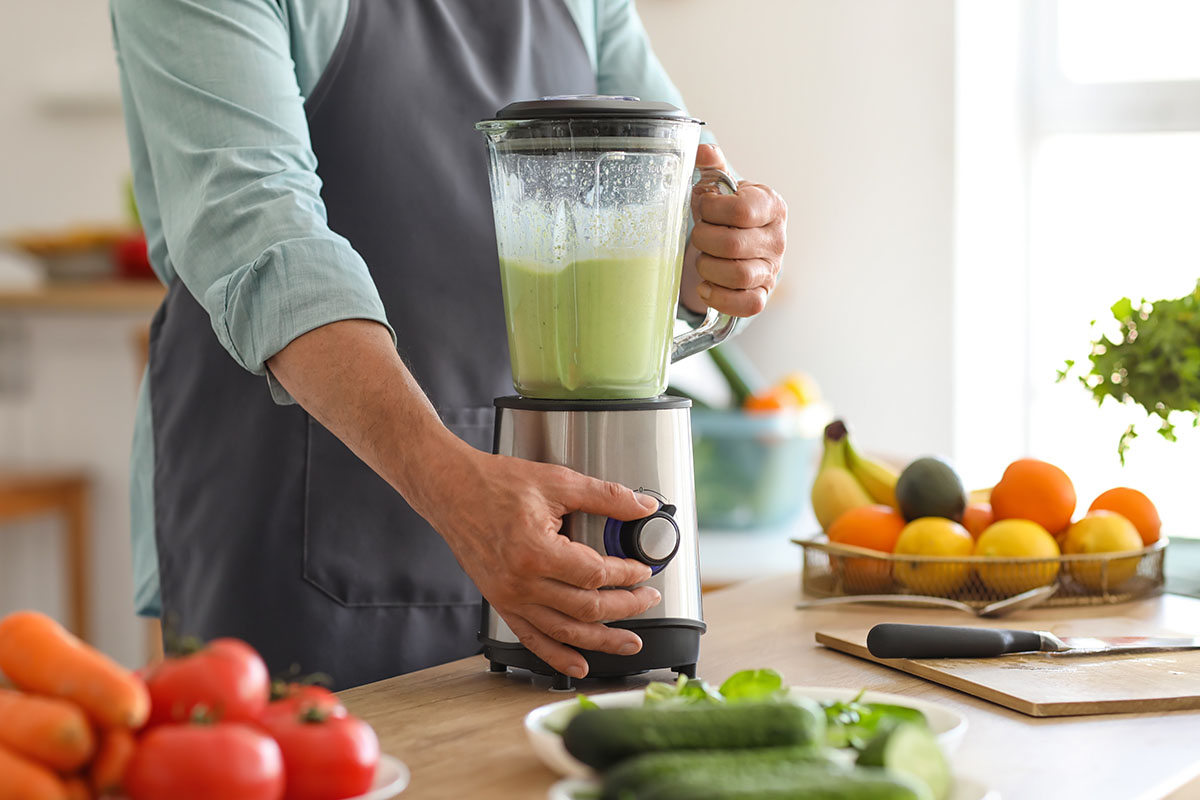 Mature man making smoothie with blender in kitchen