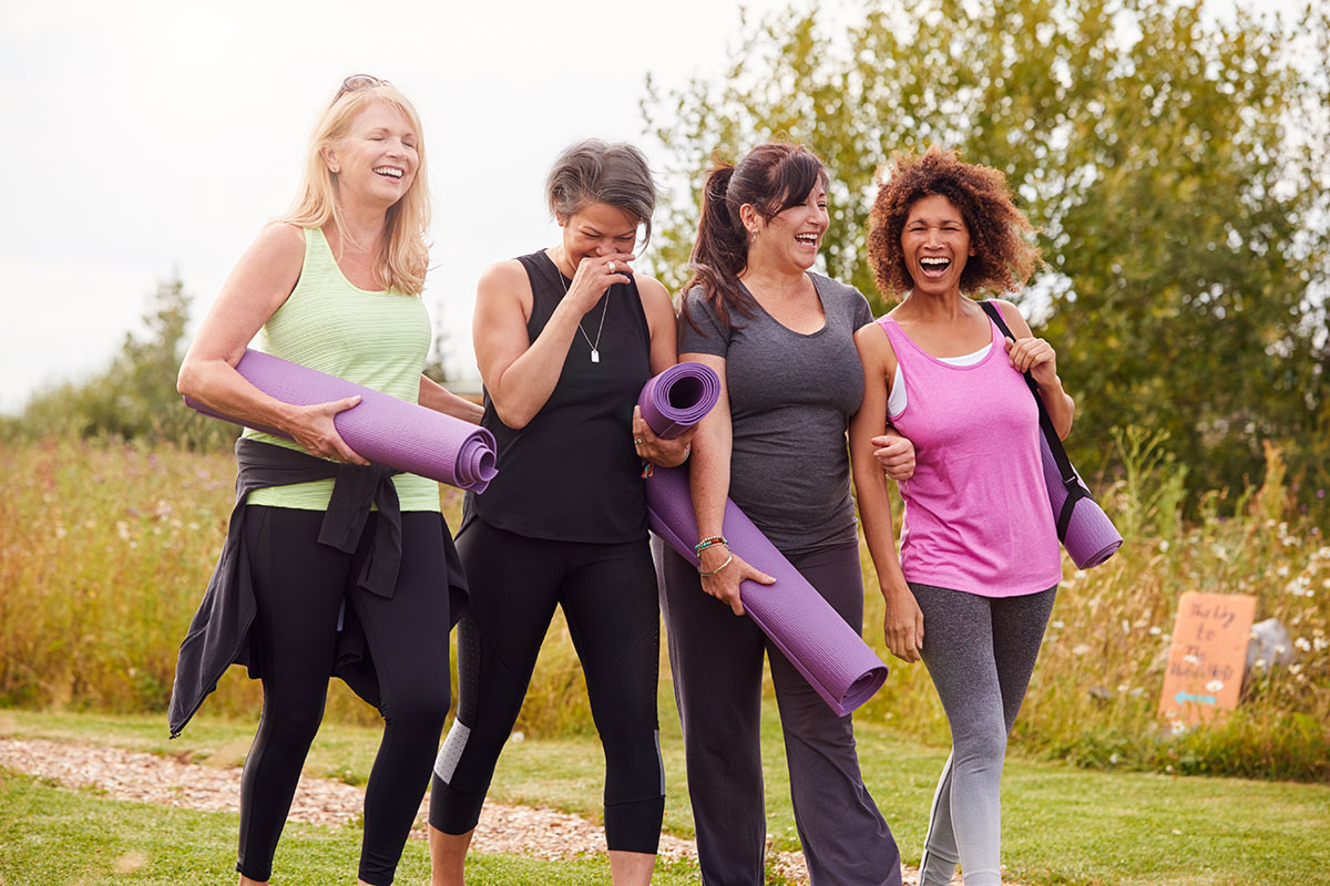 Group Of Mature Female Friends On Outdoor Yoga Retreat Walking Along Path Through Campsite