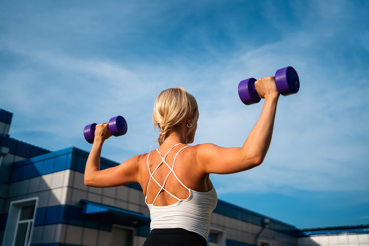 middle age woman doing weights exercises with dumbbells outdoors