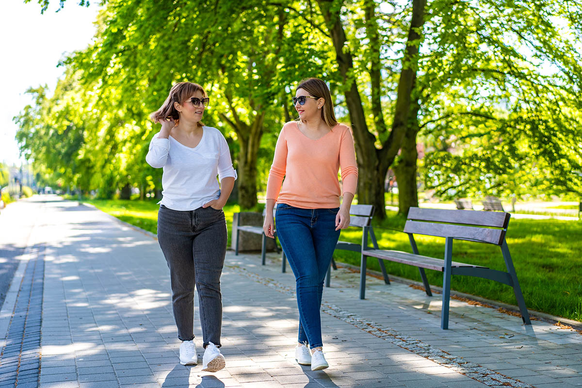 Two mid-adult women walking and talking in city park