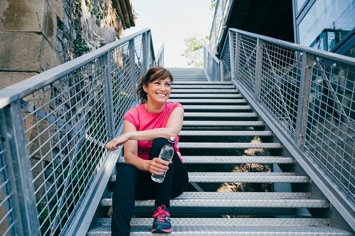 middle aged woman sitting on metallic stairs relaxing before running outdoors 