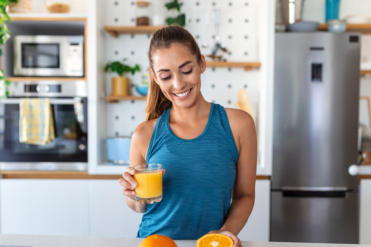 Woman drinking orange juice in kitchen. Vitamin-C supplement.